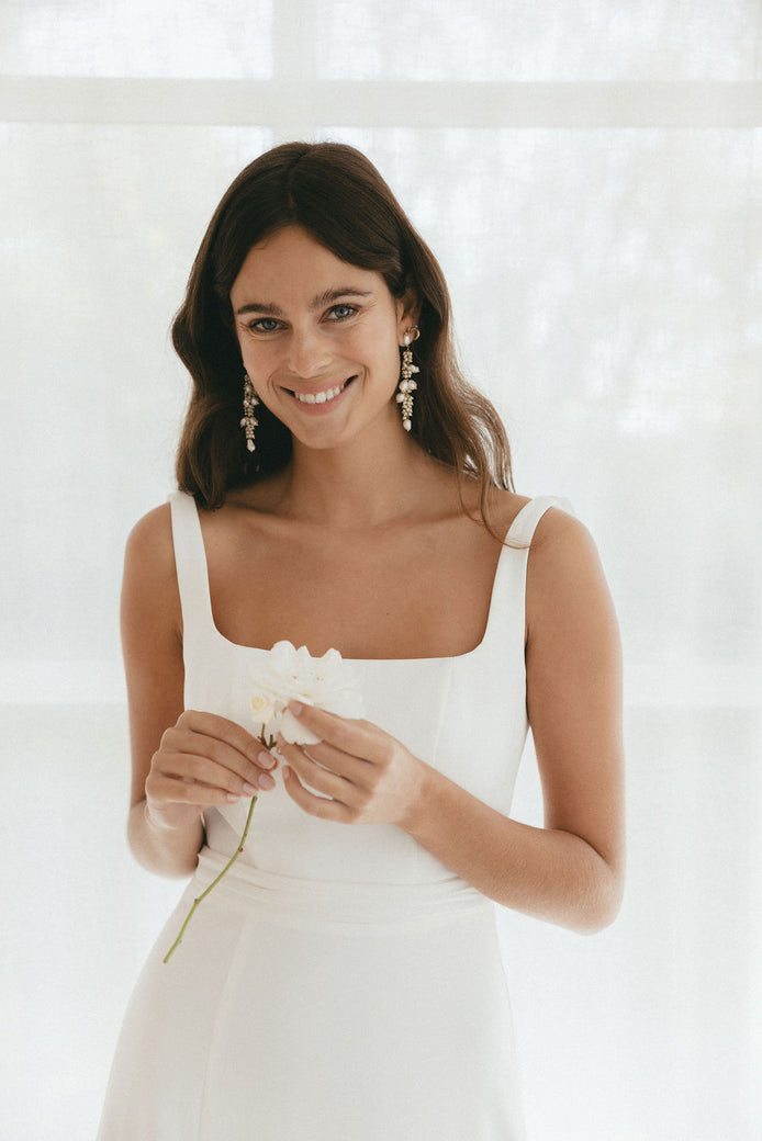 Woman wearing a white wedding dress holding a flower against a white background. She is a bride
