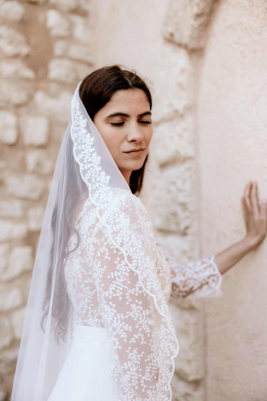 Woman wearing a lace veil against a stone wall