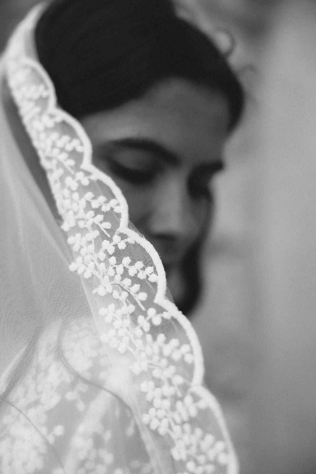 Close-up of a woman wearing a lace veil in black and white.