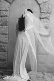 Woman wearing a long white wedding dress with a veil in front of a stone archway.