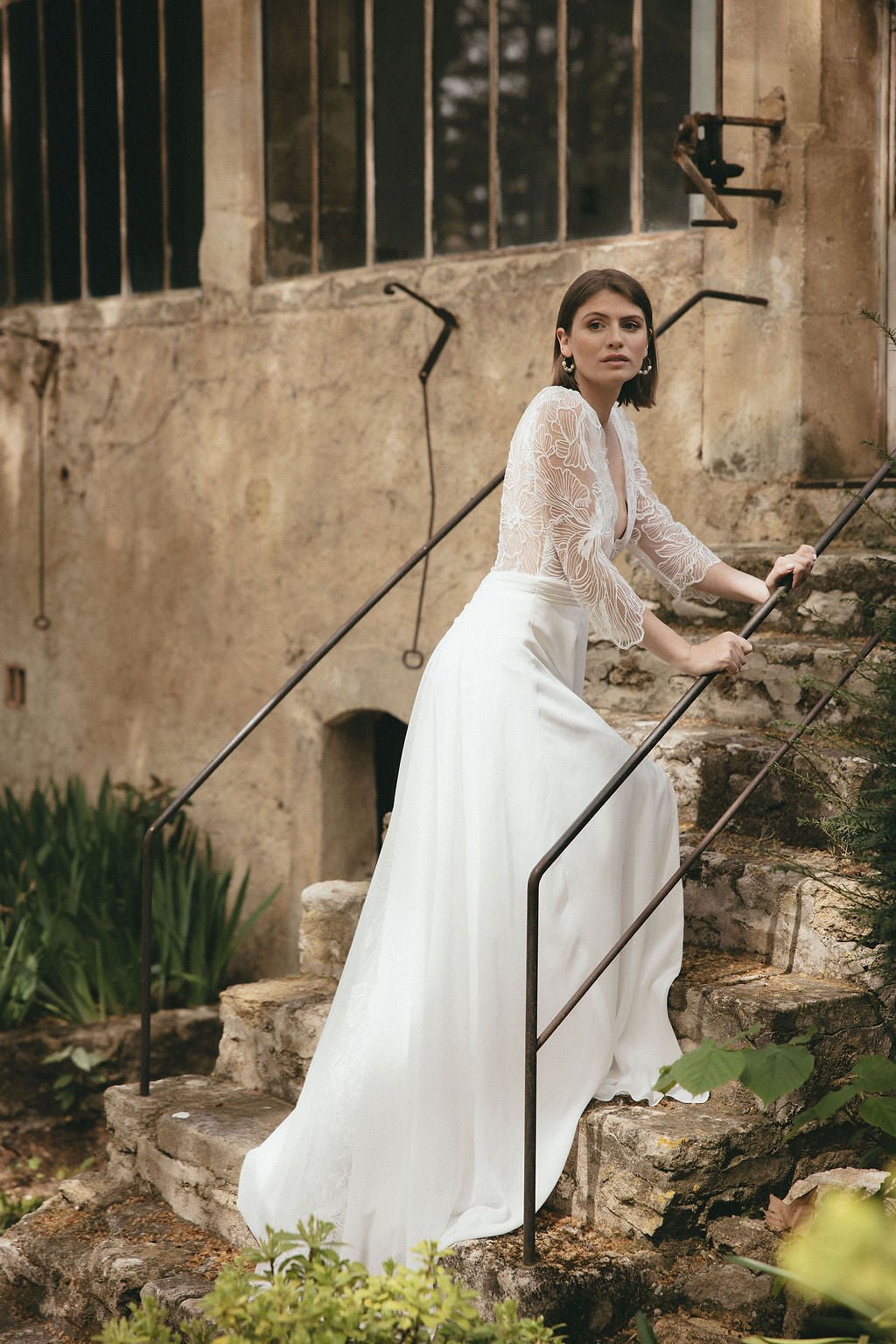 Bride wearing Ariette lace wedding dress with cap sleeves and sheer bodice, set against a natural outdoor backdrop for a soft romantic bridal look