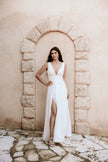 Bride in a flowing white wedding dress with thigh-high slit posing in a stone archway, capturing modern Australian bridal elegance and timeless style